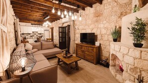 A cozy living room with a stone wall, wooden ceiling beams, a sofa, a TV, and a fireplace.