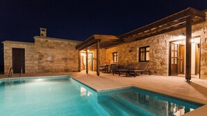 A stone building with a swimming pool, outdoor seating, and a pergola.