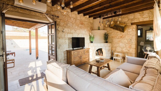 A rustic stone interior with a wooden ceiling, a flat-screen TV, a fireplace, and a sofa.