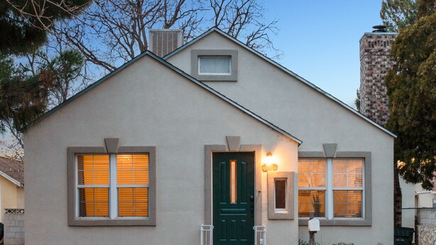 Une maison de plain-pied avec une porte verte, deux fenêtres avec des volets, un petit porche et une boîte aux lettres.
