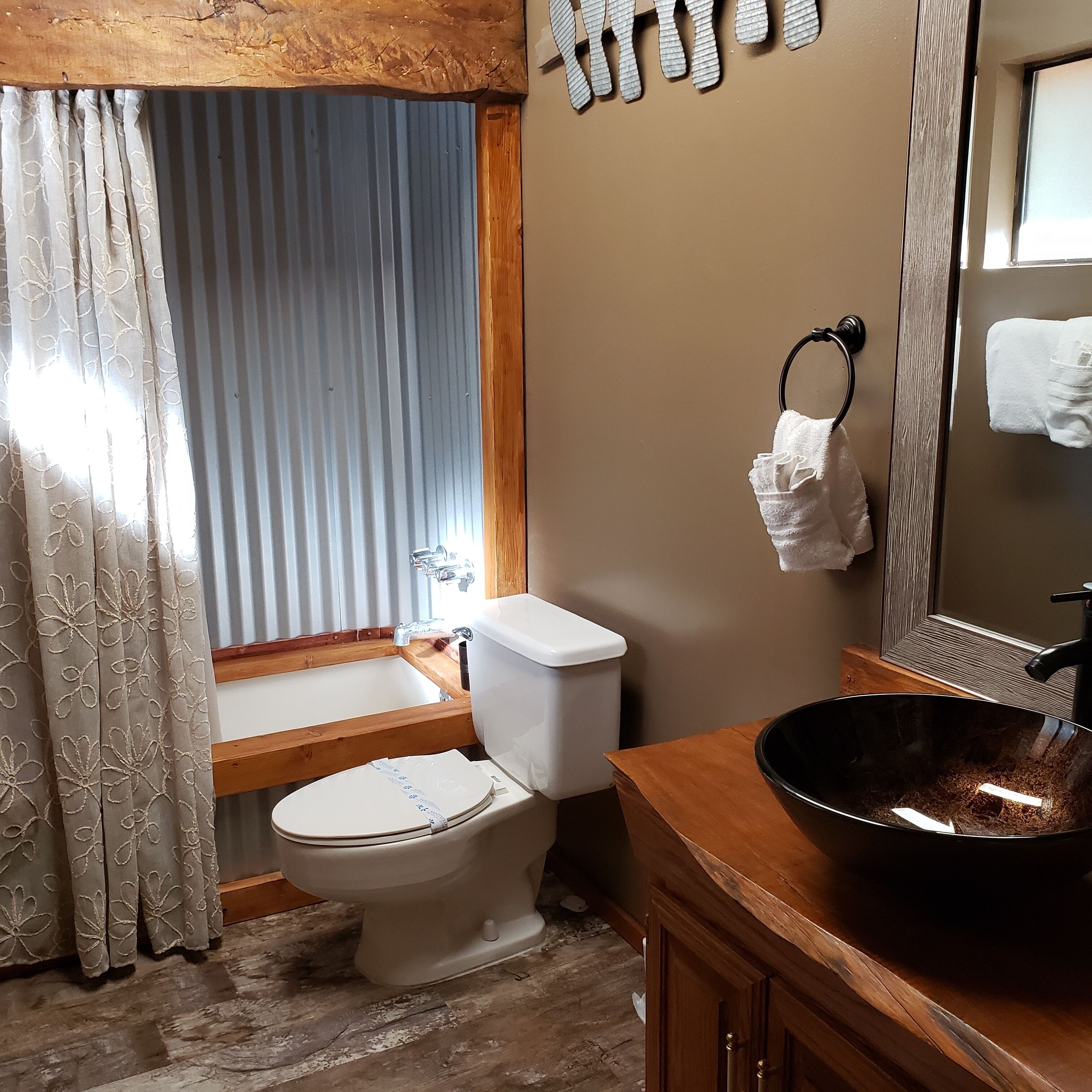 A bathroom with a wooden vanity, a toilet, a sink, and a large mirror.