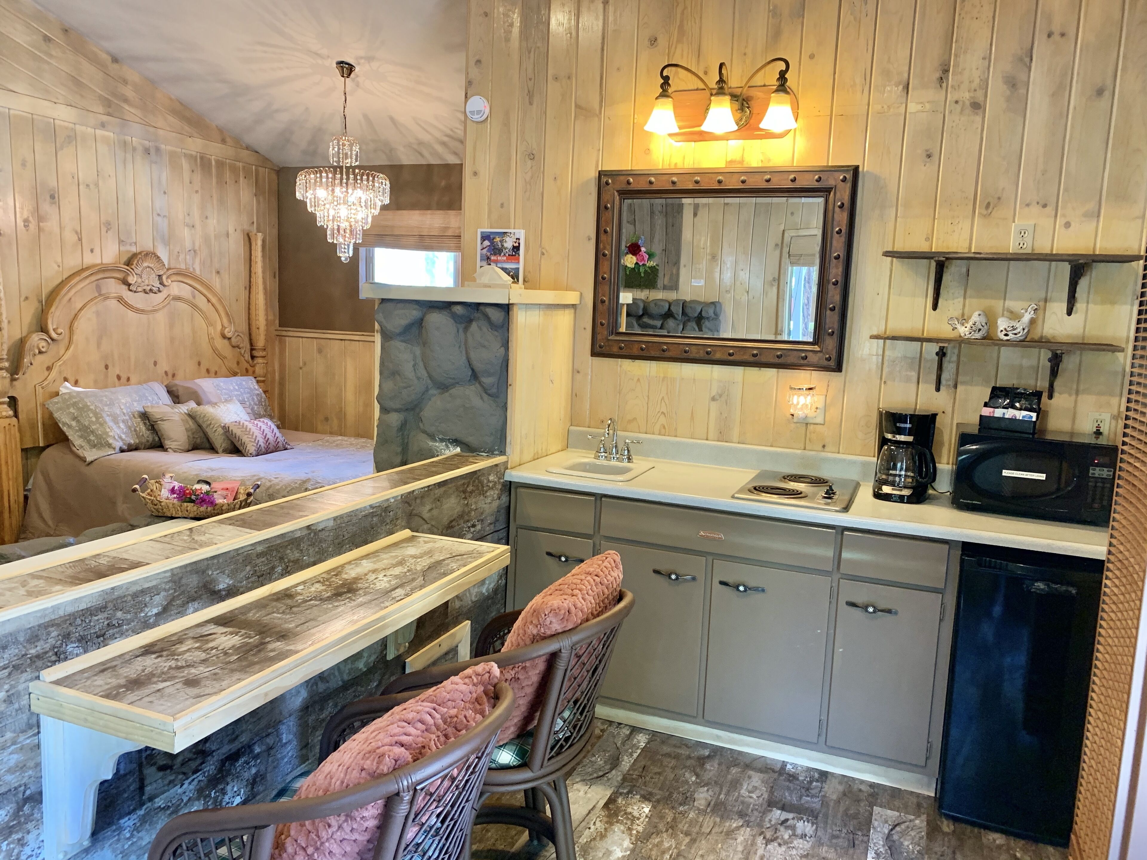 Ein Interieur einer Holzhütte mit Bett, Steinwand, Spüle, Mikrowelle und kleinem Kühlschrank.