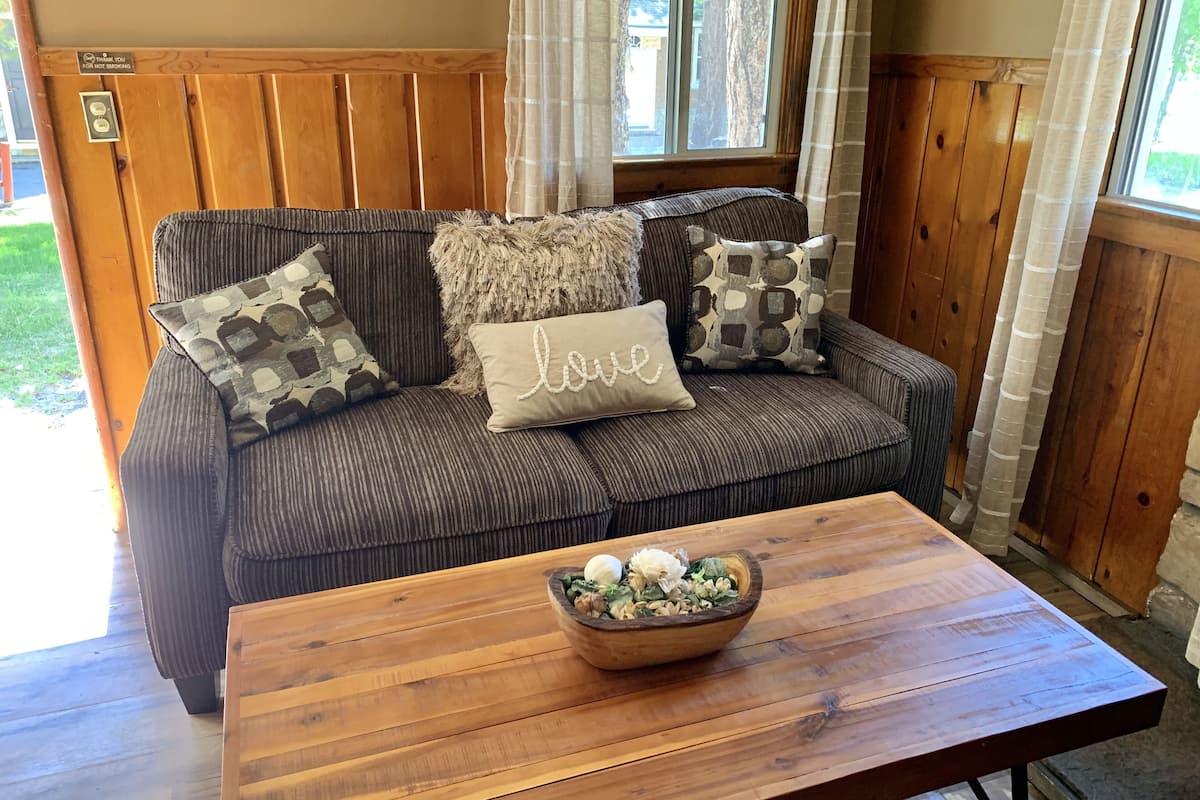 A cozy room with a wooden panel wall, a cushioned sofa with patterned pillows, and a wooden coffee table with a floral arrangement.