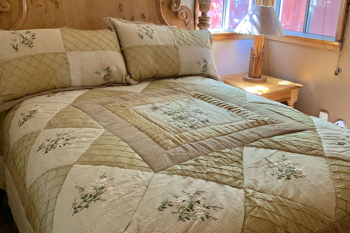 A bed with a floral quilt, a wooden headboard, and a nightstand with a lamp.