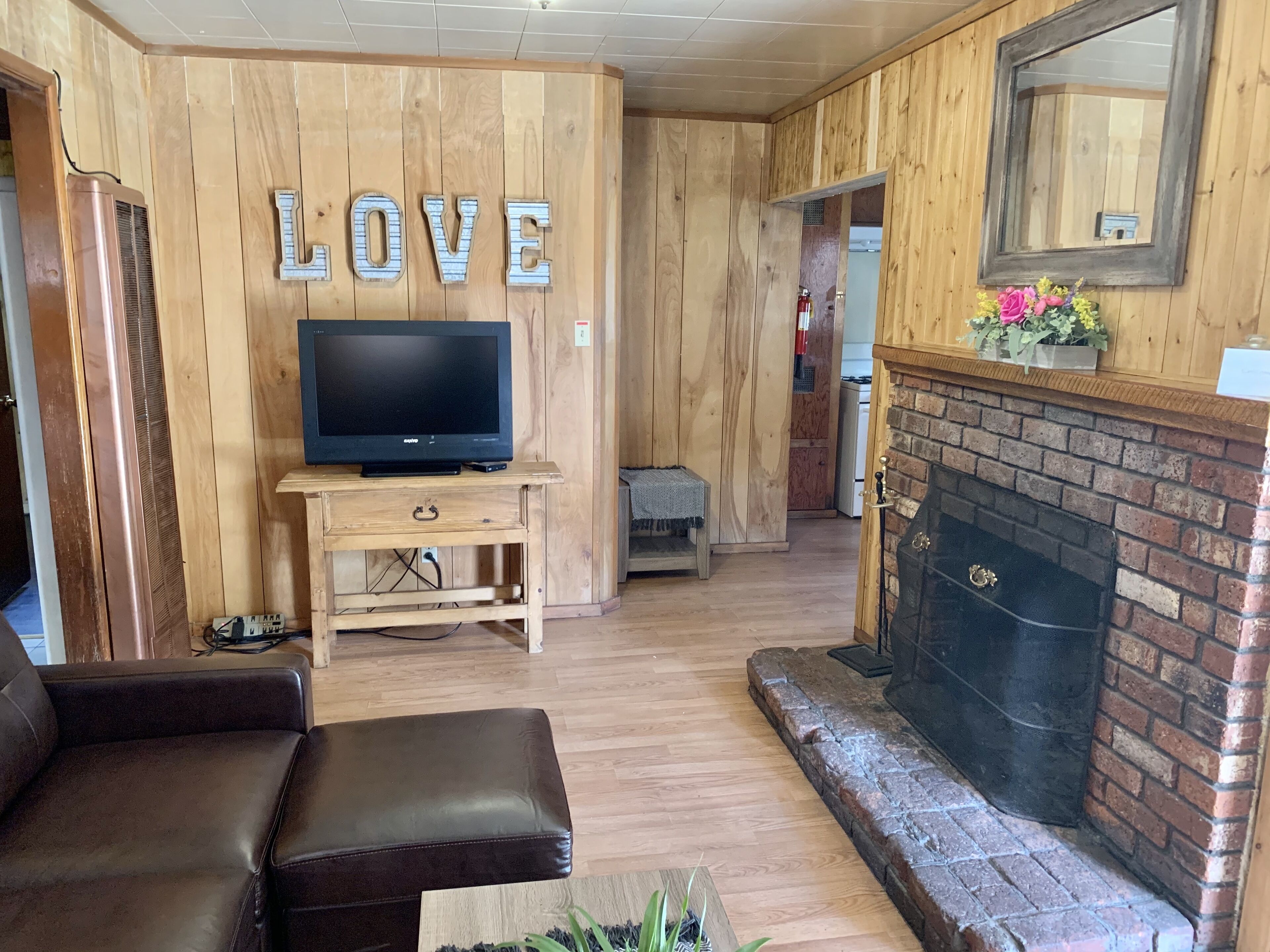 Una sala de estar acogedora con chimenea, un televisor sobre un soporte de madera y un letrero con la palabra 'LOVE'.