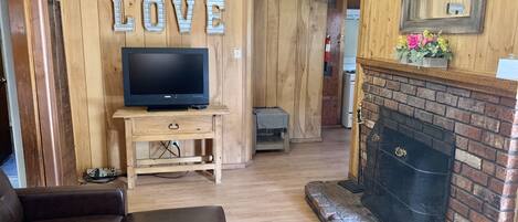 Una sala de estar acogedora con chimenea, un televisor sobre un soporte de madera y un letrero con la palabra 'LOVE'.