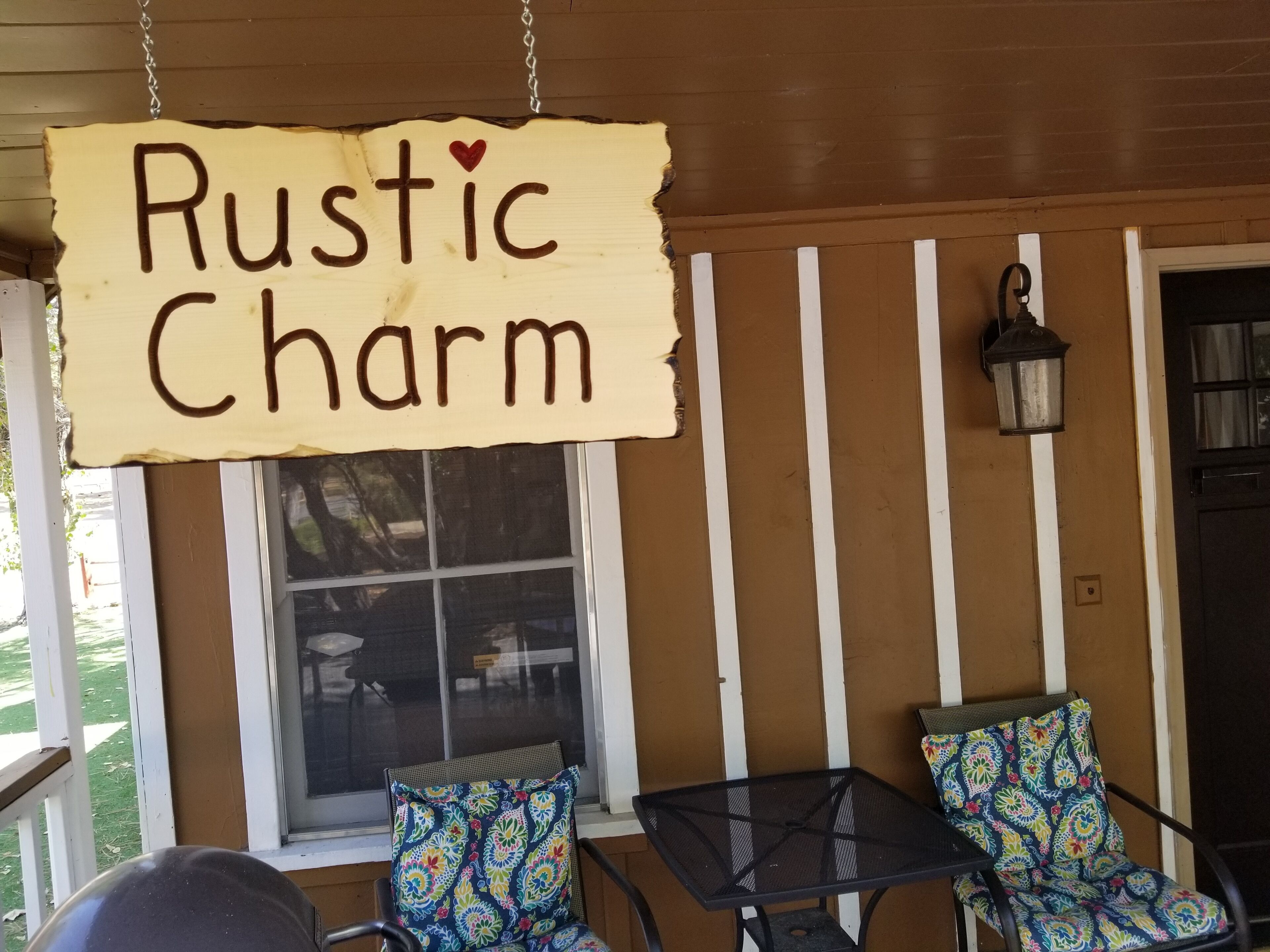 A porch with a sign reading "Rustic Charm" and two chairs with patterned cushions.