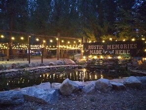 A rustic outdoor setting with a pond, wooden structures, and string lights. - Grey Squirrel Resort (Big Bear Lake)