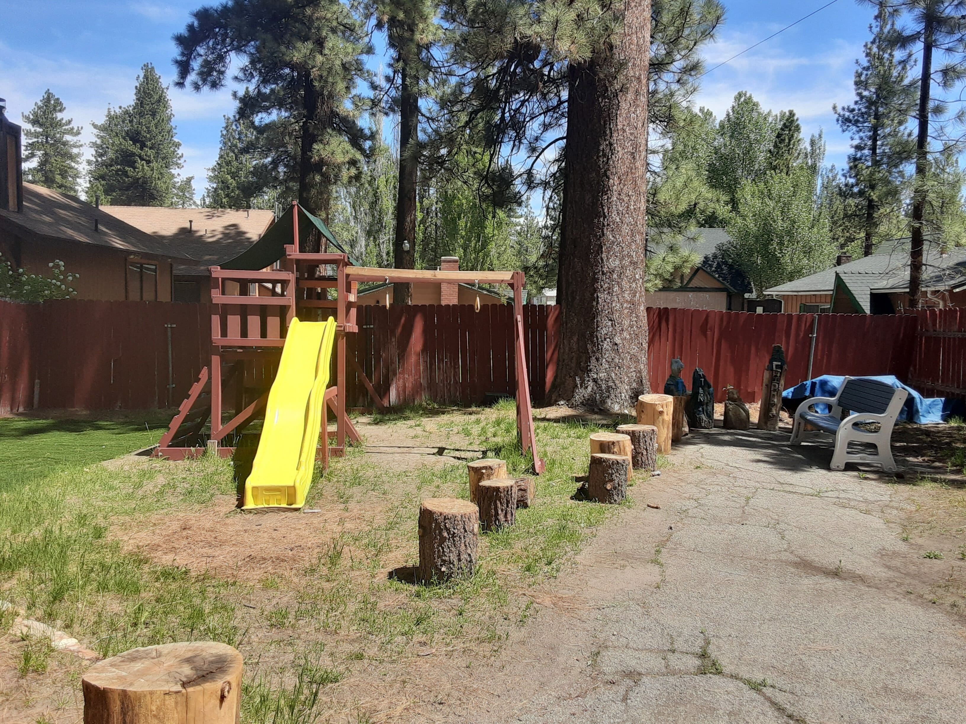 A backyard with a wooden playset, including a slide, and a red fence.