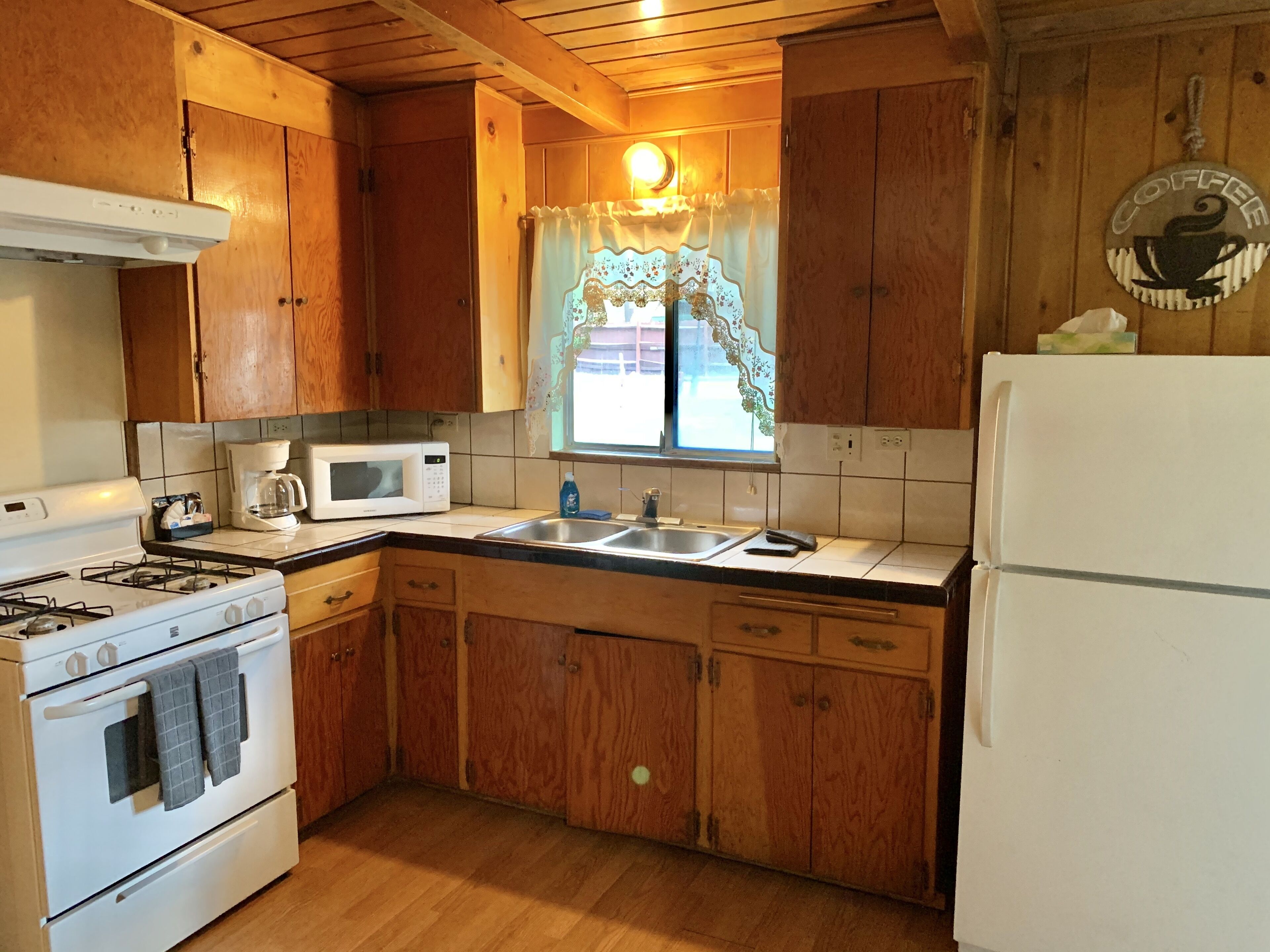 A kitchen with wooden cabinets, a white stove, a microwave, and a refrigerator.