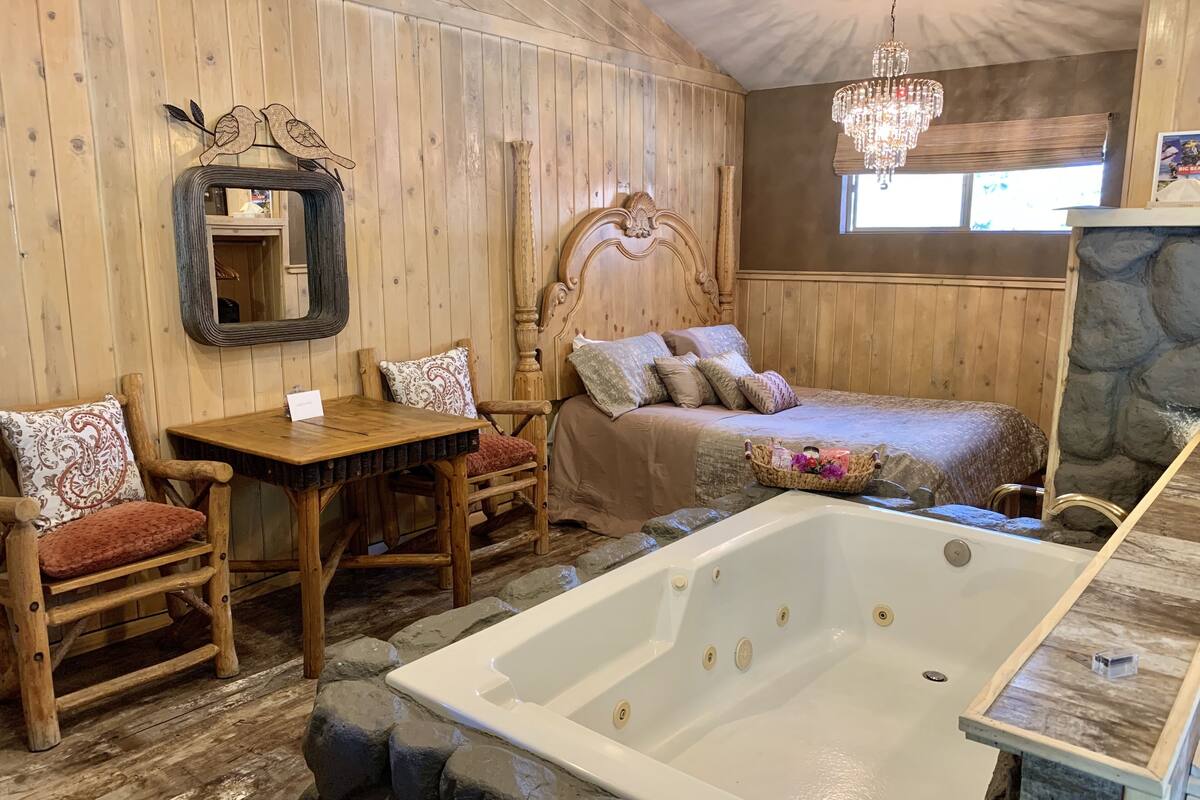 A wooden room with a large bathtub, a wooden table, and a bed with multiple pillows.