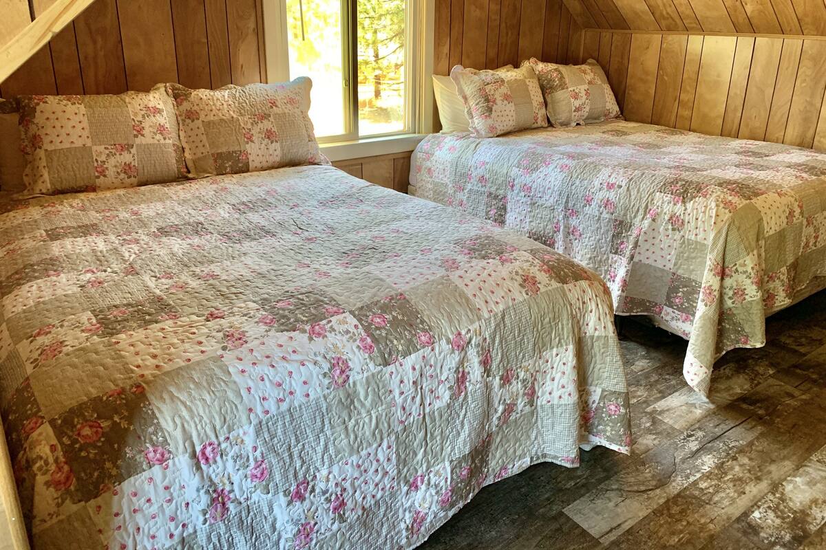 A cozy attic bedroom with two beds, wooden walls, and a large window.