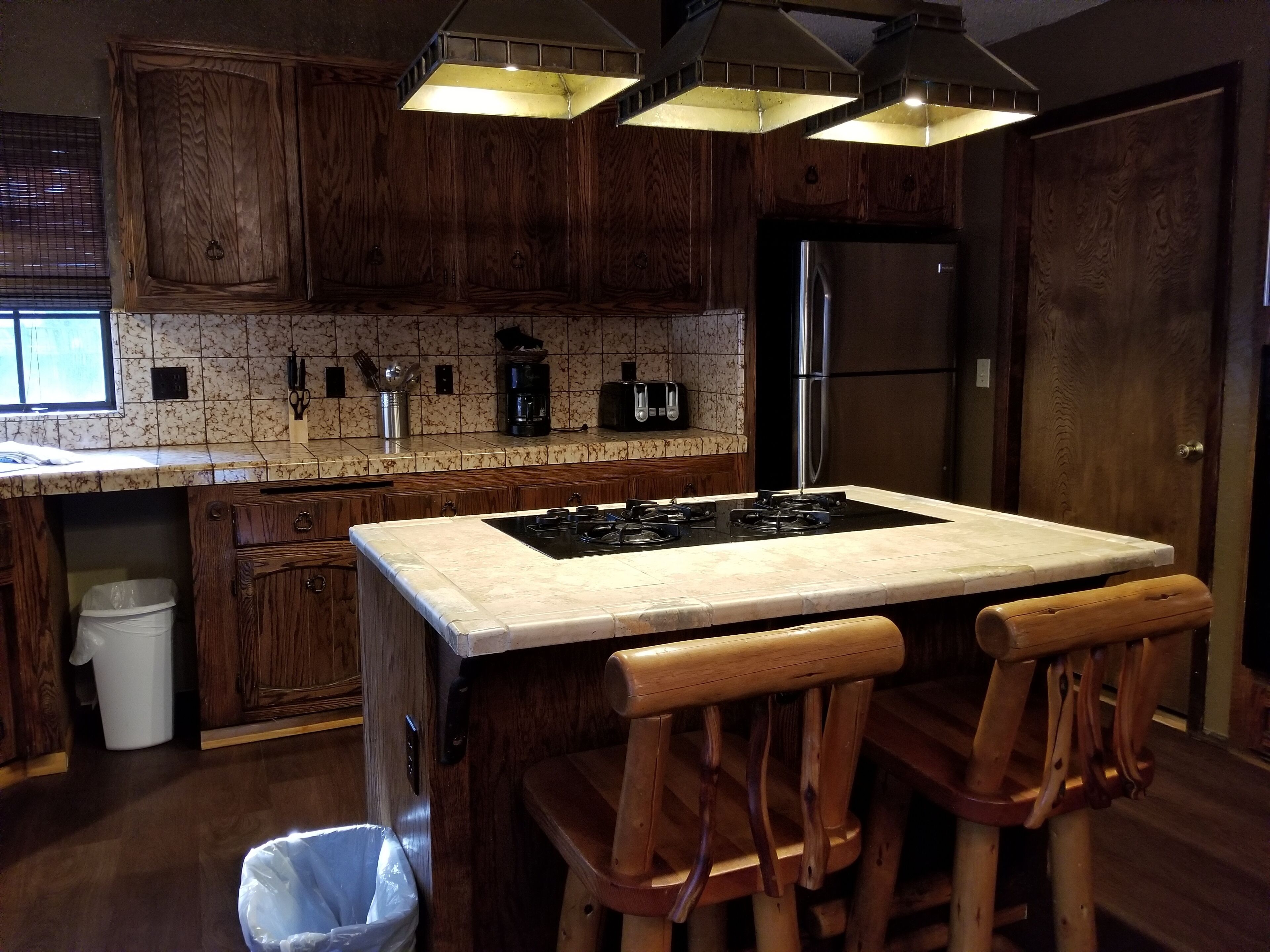 A kitchen with wooden cabinets, a marble countertop, a gas stove, and a refrigerator.