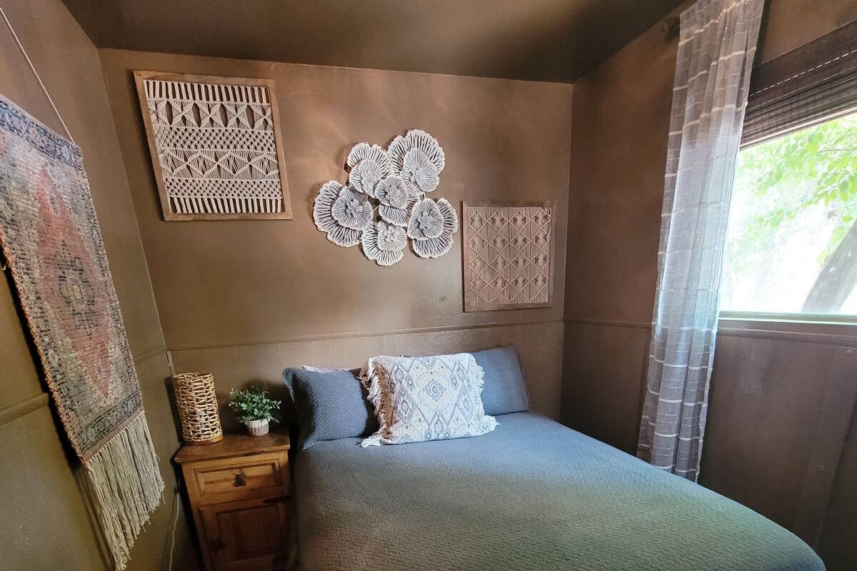A bedroom with a bed, a nightstand, a wall hanging, and a window with curtains.