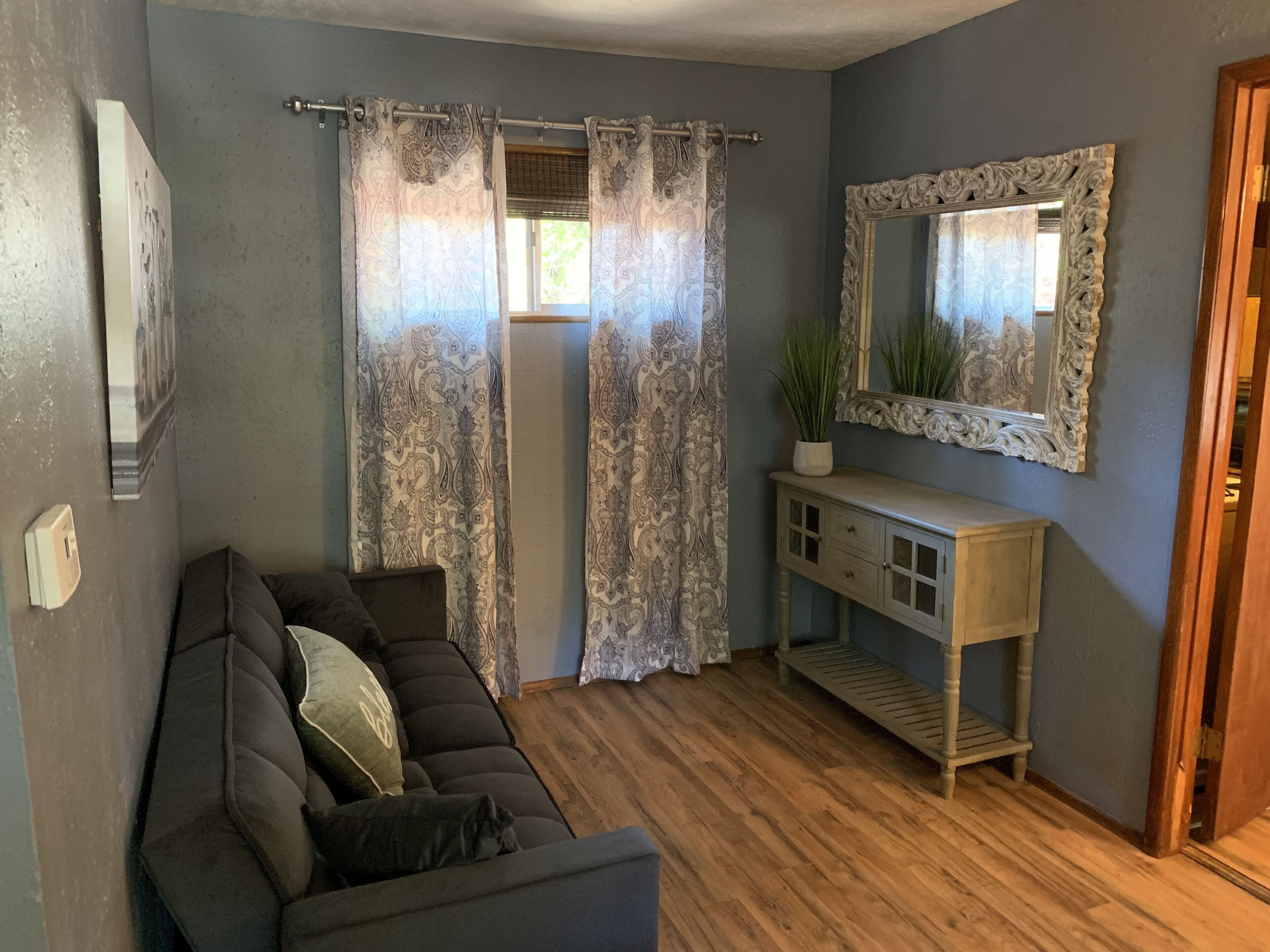 Un salon avec un canapé de couleur sombre, une console en bois et un miroir doté d’un cadre orné.