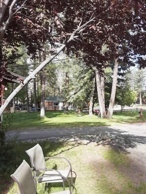 A park with a paved path, two metal chairs, and a building in the background. - Grey Squirrel Resort (Big Bear Lake)
