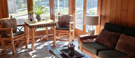 A wooden interior with a sofa, chairs, a table, and a window with blinds.