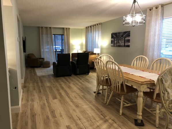 A dining area with a wooden table and chairs, a sofa, and a lamp. - Prime Location! 2BR Condo w/ Heated Indoor Pool - Walk to Beach & Dining (Myrtle Beach)