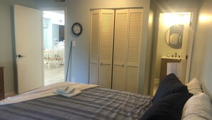 Een slaapkamer met een bed, een kledingkast, een klok en een zichtbare badkamer door een geopende deur.