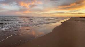 Une plage avec une mer calme et un ciel au coucher du soleil.