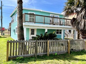 Stunning two-story home with a front porch and staircase, surrounded by a wooden fence and a palm tree.