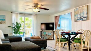 Un salon comprenant un canapé, une table à manger avec des chaises, un téléviseur et un ventilateur de plafond.