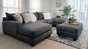 Un salon moderne avec un canapé d’angle, un pouf et un plateau décoratif.