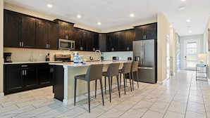 Una cocina moderna con muebles oscuros, un refrigerador de acero inoxidable, un microondas y una cafetera.