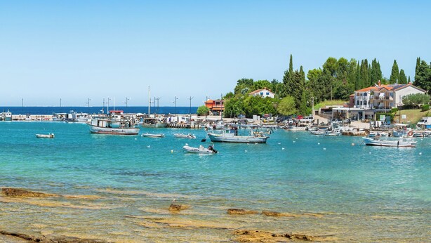 A coastal marina with boats docked, clear turquoise water, and buildings with red roofs.