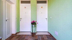 A hallway with two white doors, a potted plant with pink flowers, and a light green wall.