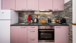 A kitchen with pink cabinets, a stone backsplash, and stainless steel appliances including a coffee maker, kettle, and toaster.