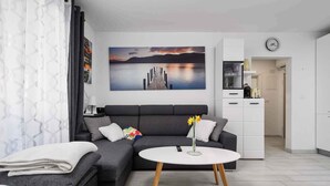 A modern living room with a grey sofa, a white coffee table, and a painting of a lake.