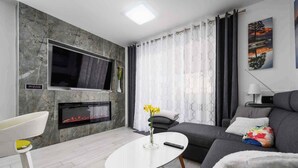 A modern living room with a flat-screen TV, fireplace, sofa, and a white coffee table.