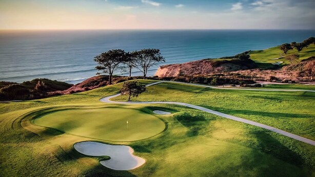 Un parcours de golf avec un obstacle d’eau, un bunker de sable et un mât de drapeau.