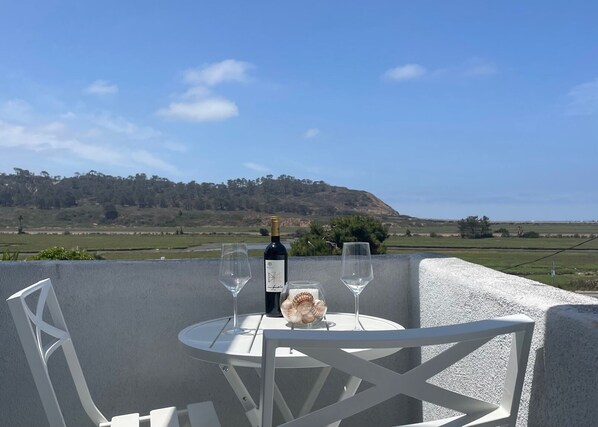 A table with a bottle of wine and two glasses, set against a scenic view of a hilly landscape.