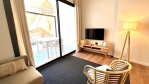 A modern living room with a sofa, a wicker chair, a TV on a wooden stand, and a floor lamp.
