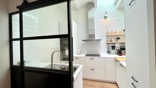 A modern kitchen with white cabinetry, a black-framed sliding door, and a visible kitchen island.