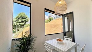 A dining area with a table and chairs, a potted plant, and a view of a hillside through large windows.