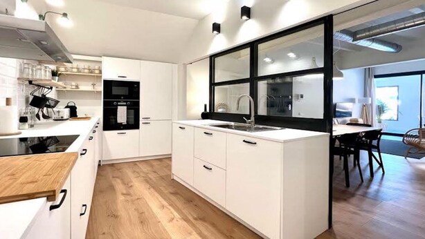 Een moderne keuken met witte kasten, een zwart aanrecht en een groot raam.