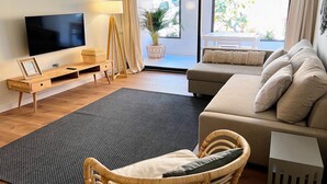 Een moderne woonkamer met een flatscreen televisie, een houten console, een rieten stoel en een bank met kussens.