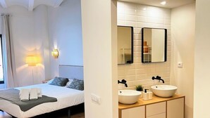 Een moderne hotelkamer met een bed, bedlampen, een grote spiegel en een houten wastafel.