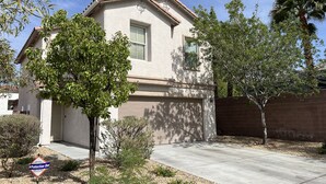 A single-story house with a beige exterior, a front garage, and a small front yard with trees and shrubs.