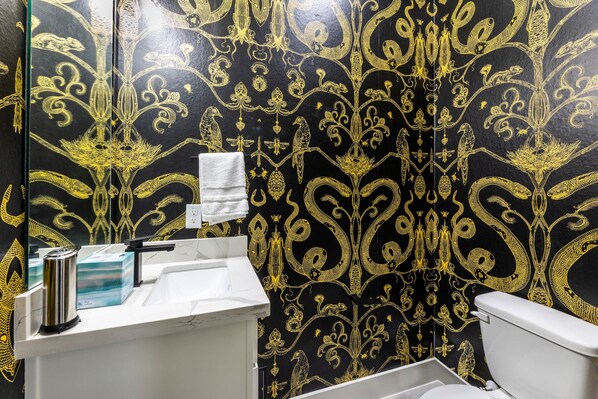 A bathroom with a black and gold patterned wall, a white sink, and a toilet. - Luxury Smart Home Less Than A Hour From Houston (Dayton)