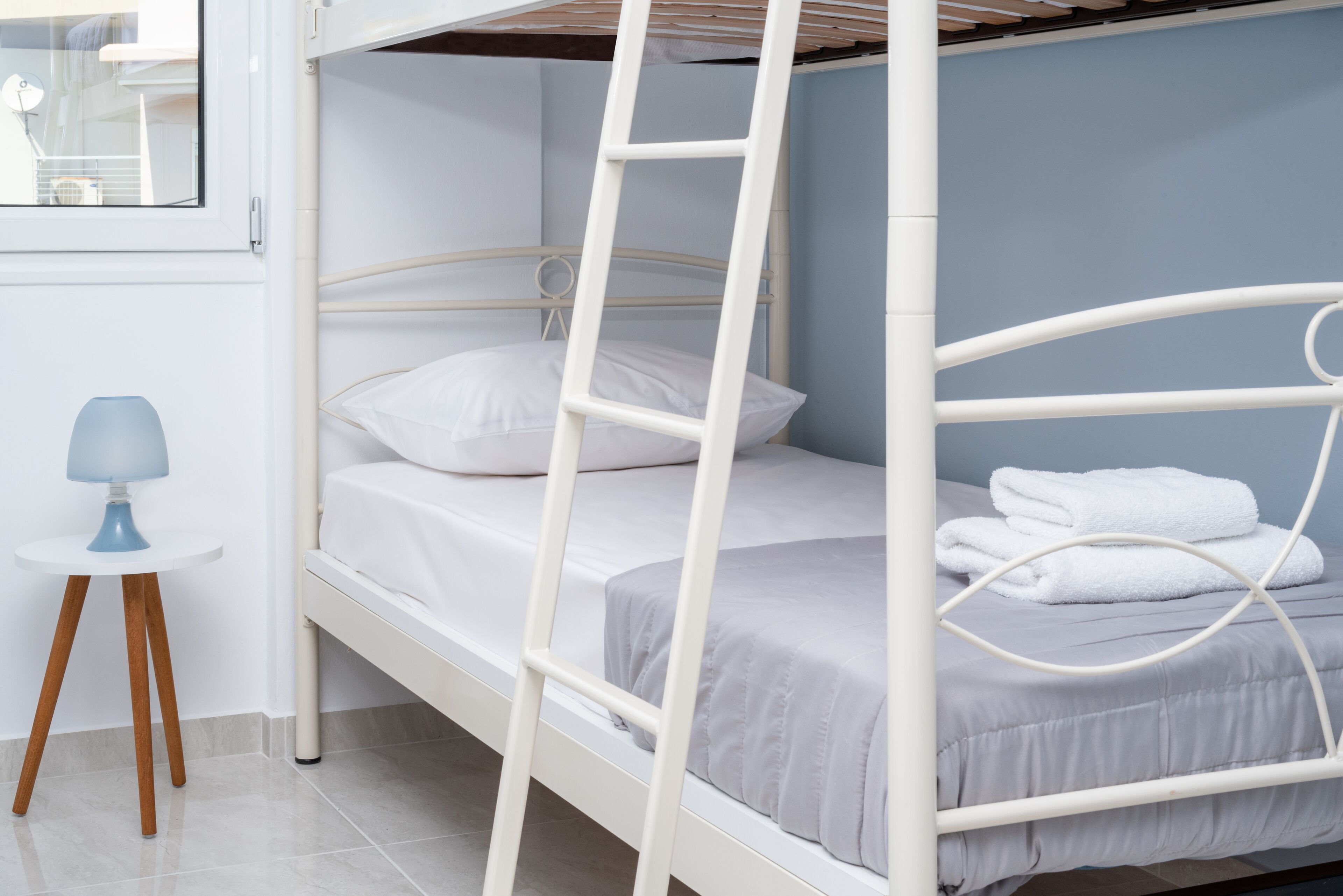 A bunk bed with a ladder, a small table with a lamp, and a window.