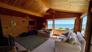 A cozy cabin interior with a large sofa, a small table, and a view of the sea. - Absolute beachfront Raumati (Paraparaumu)