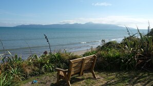 A wooden bench overlooking a beach with a view of the ocean and distant mountains. - Absolute beachfront Raumati (Paraparaumu)