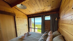 A wooden cabin bedroom with a bed, pillows, and a view of the outdoors. - Absolute beachfront Raumati (Paraparaumu)