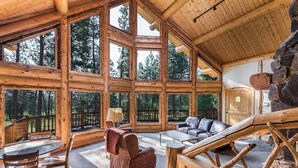 A spacious wooden cabin with large windows, a cozy seating area, and a stone fireplace. - Pineview Lodge (Hamilton)