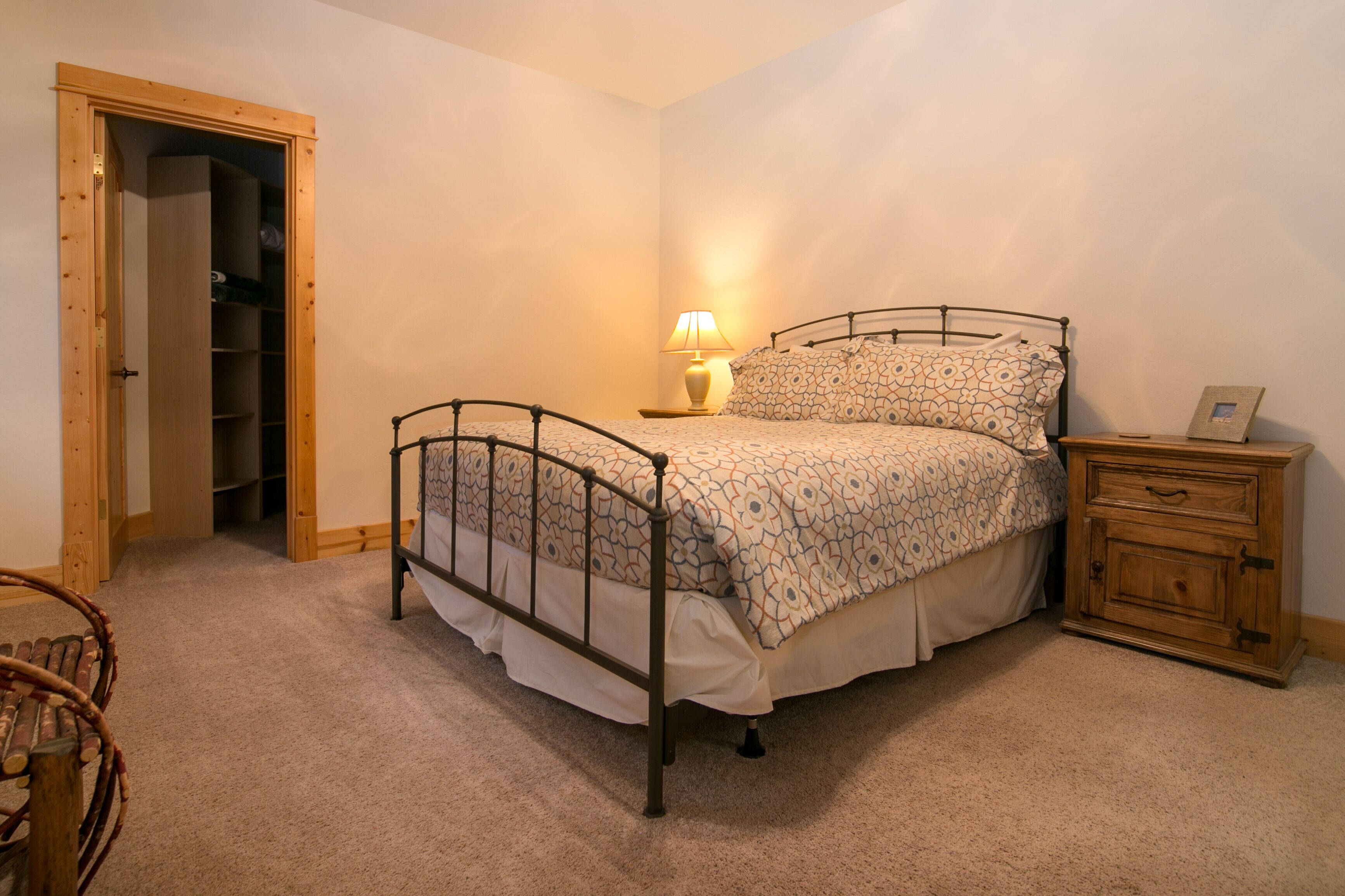 Een slaapkamer met een metalen bedframe, een nachtkastje met een lamp, een houten nachtkastje en een houten garderobe.