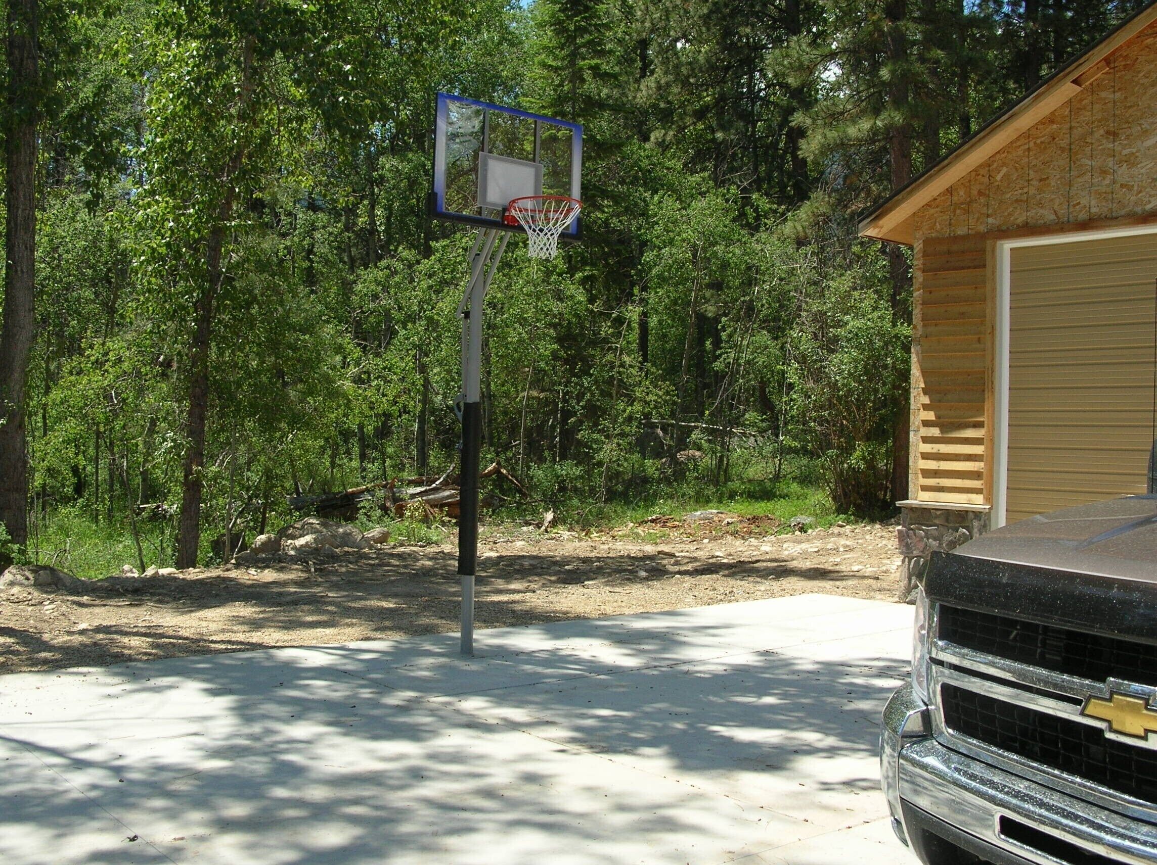 Una canasta de baloncesto en un área boscosa con un garaje y una camioneta al frente.
